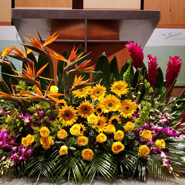 Large tropical stage arrangement with yellow sunflowers, roses, birds of paradise, orchids, and red ginger