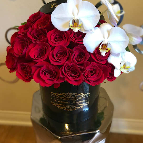 Red roses and white orchids arranged in a black hatbox