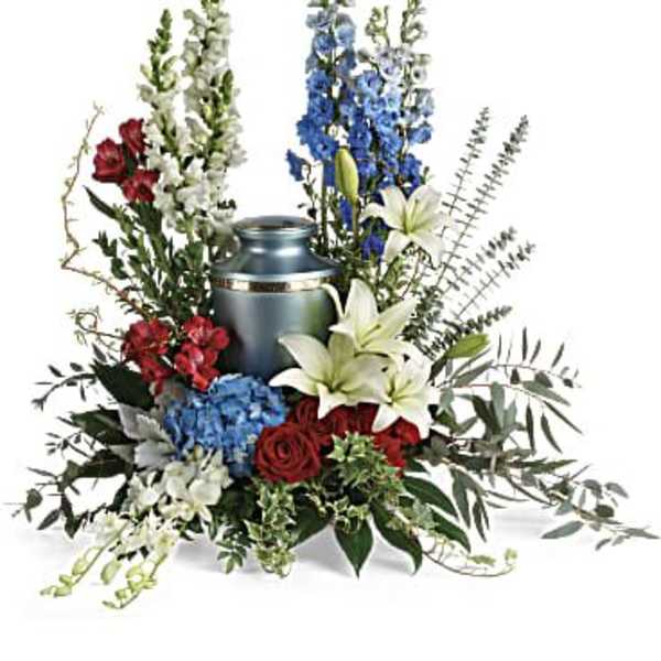 Floral funeral urn arrangement with lilies, roses, and tall blue spikes