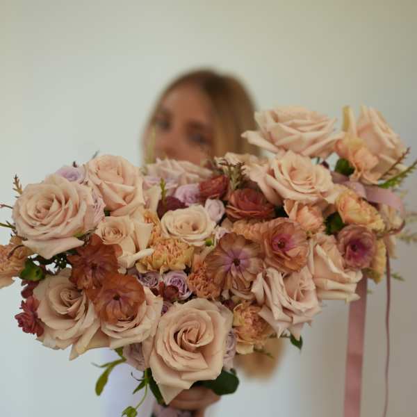 Large bouquet of blush roses and peach flowers tied with pink ribbon