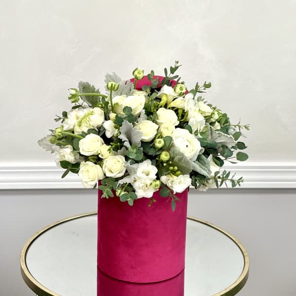 White roses and small white blooms in a pink cylindrical box