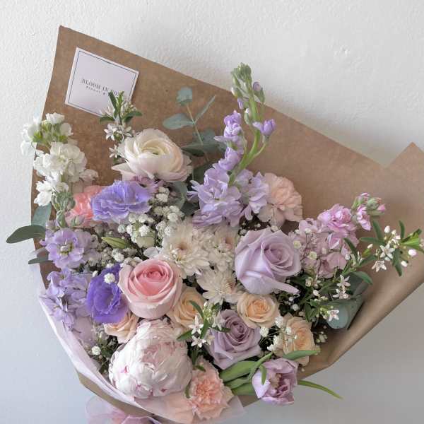 Pastel bouquet of roses, peonies, and lavender flowers wrapped in brown paper
