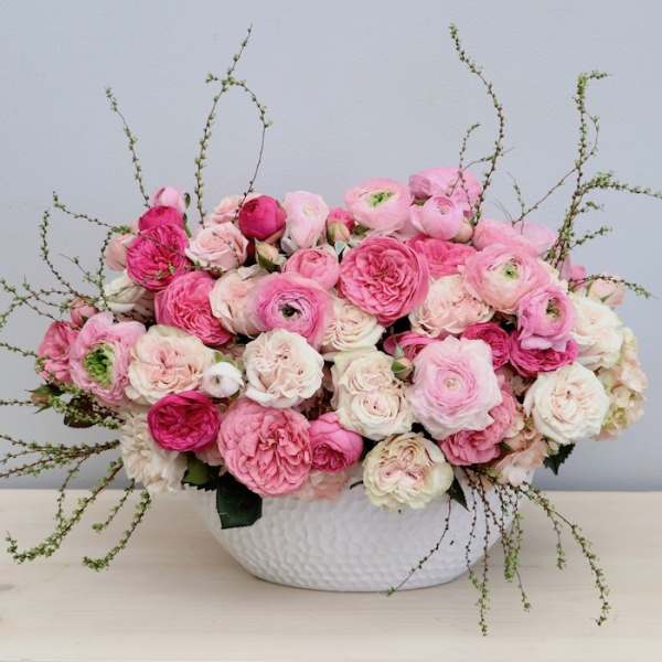 Low arrangement of pink and white roses and ranunculus in a white textured bowl