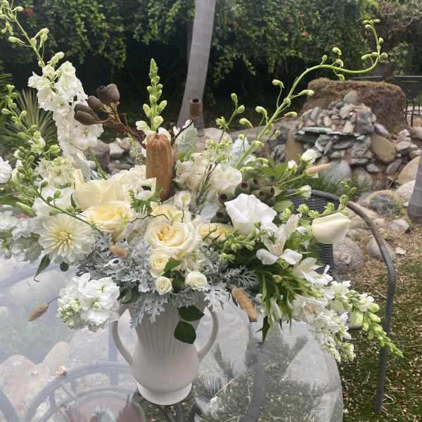 White floral arrangement in a white vase with cream roses and tall white blooms