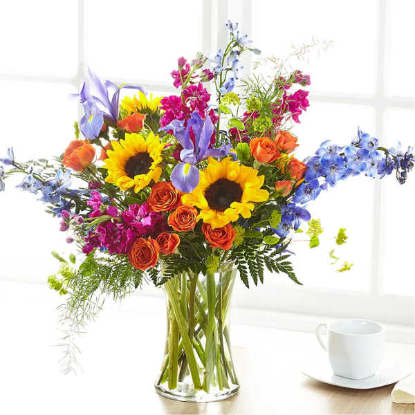 Mixed bouquet with sunflowers, roses, irises, and blue flowers in a glass vase