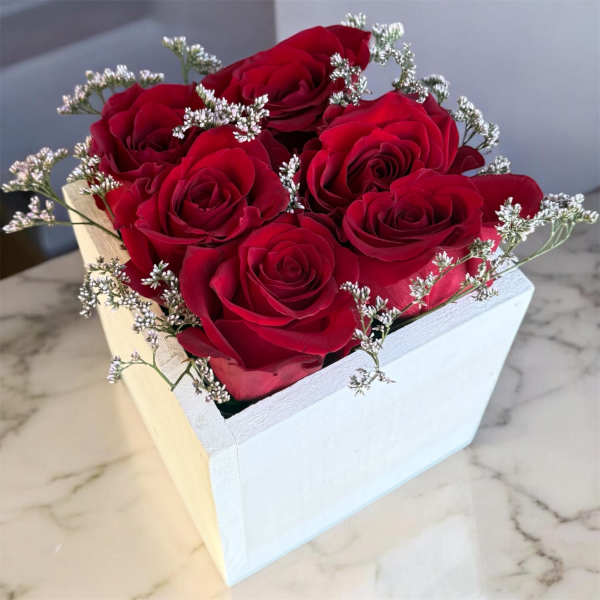Red roses arranged in a white square box with small white filler flowers.