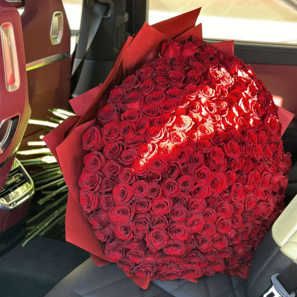 Large bouquet of red roses wrapped in red paper on a car seat