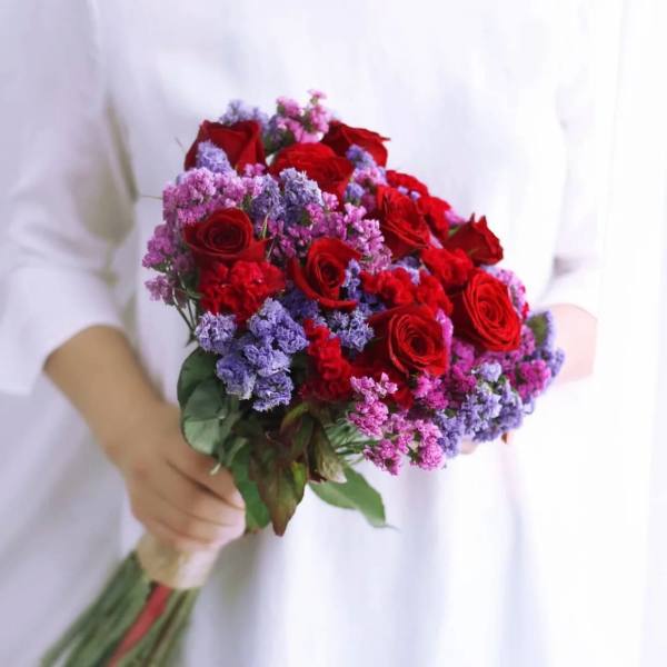 Handheld bouquet of red roses with purple and pink filler flowers