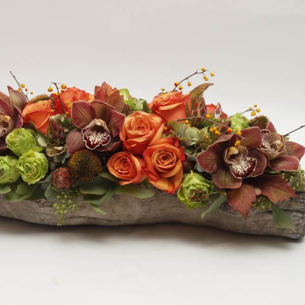Low floral arrangement with orange roses and burgundy orchids in a rustic wood container
