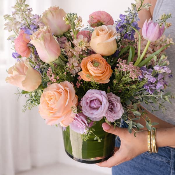 Pastel mixed bouquet of roses, tulips, and purple flowers in a glass vase