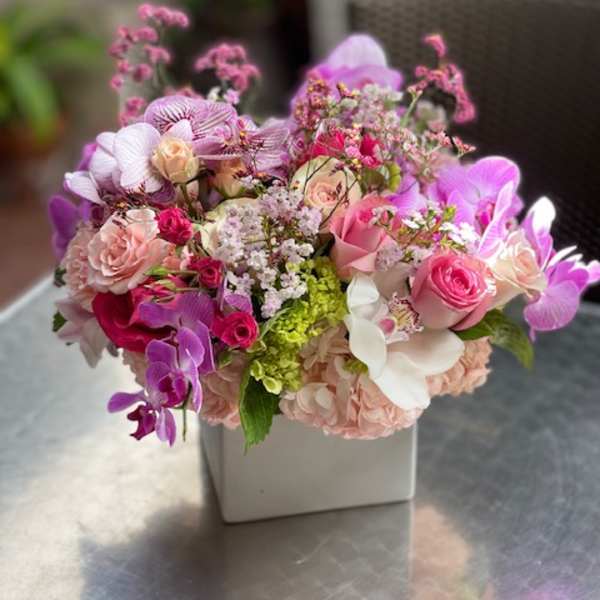 Pink and purple mixed flower arrangement in a white square vase