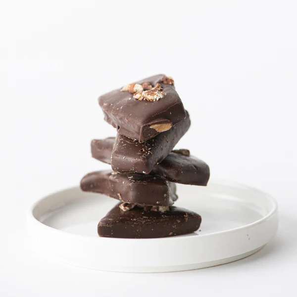 Stack of dark chocolate bark pieces with nuts on a small white plate