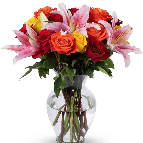 Mixed bouquet of red, orange and yellow roses with pink lilies in a clear glass vase