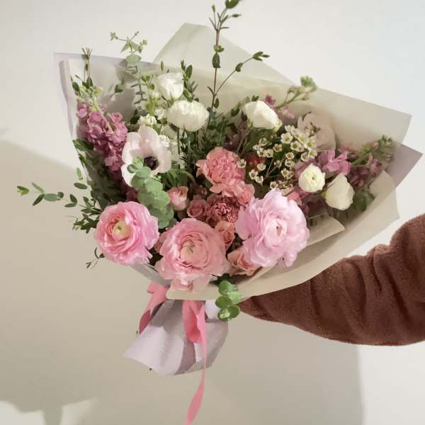 Handheld bouquet of pink and white flowers wrapped in paper