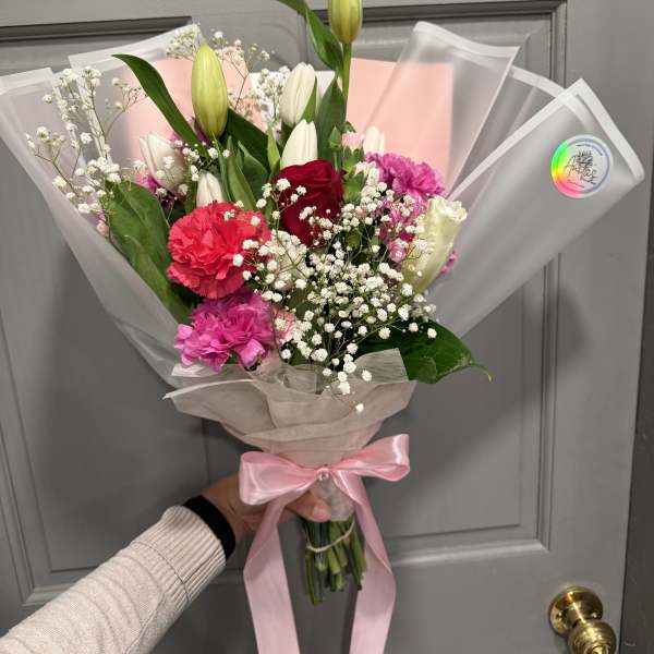 Handheld bouquet of lilies, roses, carnations, and baby's breath wrapped in pink paper