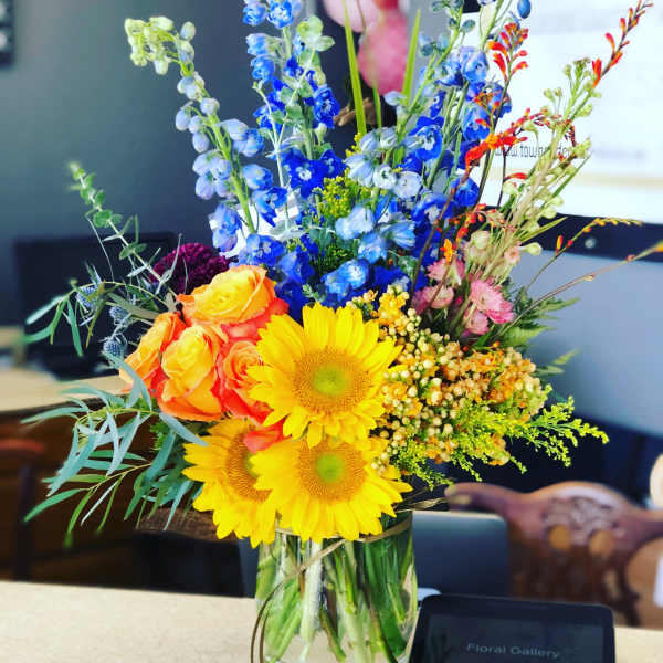 Colorful mixed bouquet in a clear glass vase with sunflowers and roses