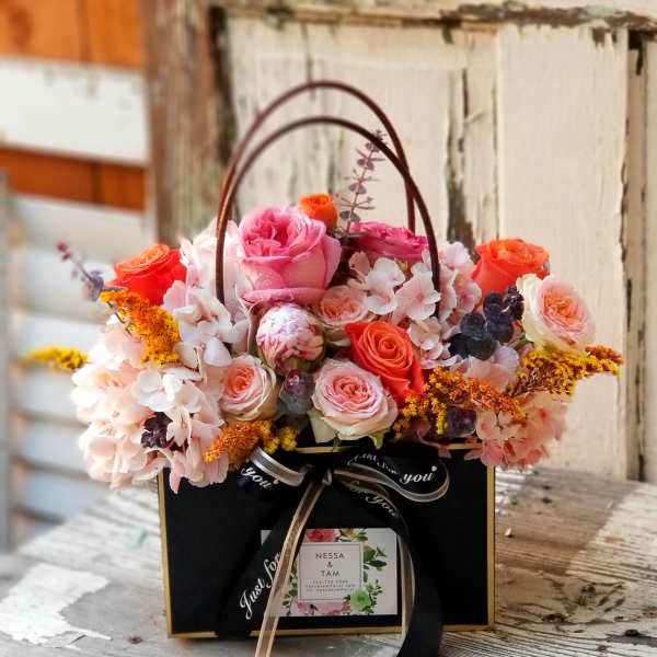 Pink and orange roses arranged in a black gift box with a handle