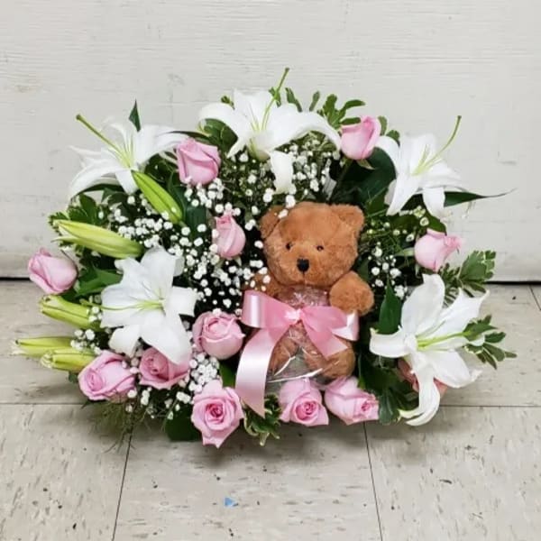 Low pink rose and white lily arrangement with a teddy bear and pink ribbon in the center