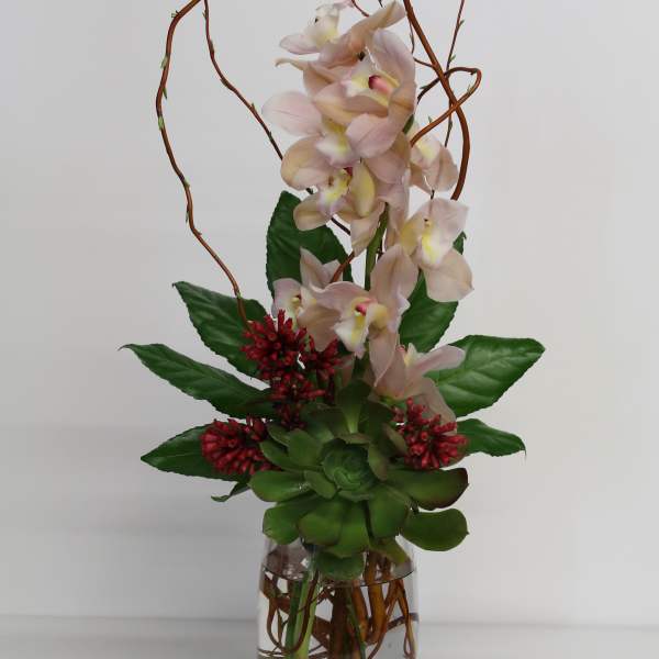 Tall arrangement of pale pink orchids, red blooms, and green succulent in a clear glass vase