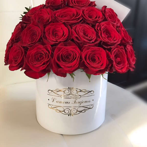 Round white hatbox of red roses with a small card on a white seat