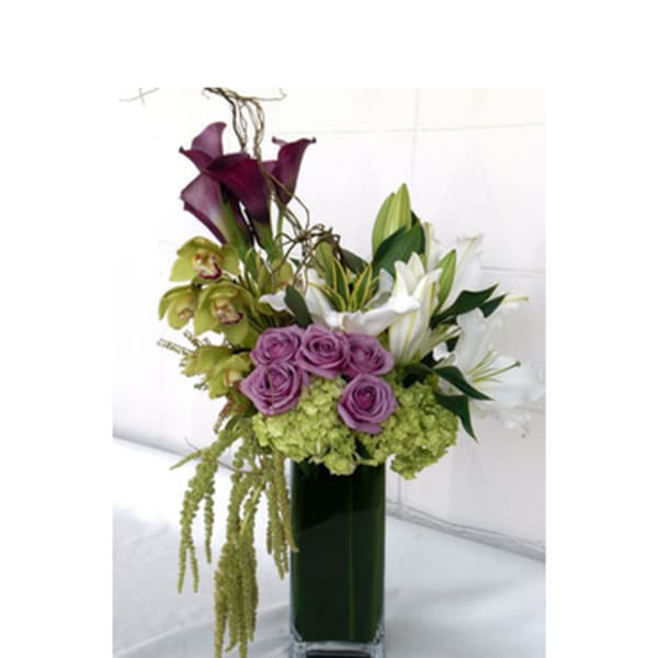 Purple roses, white lilies, and green orchids in a tall glass vase