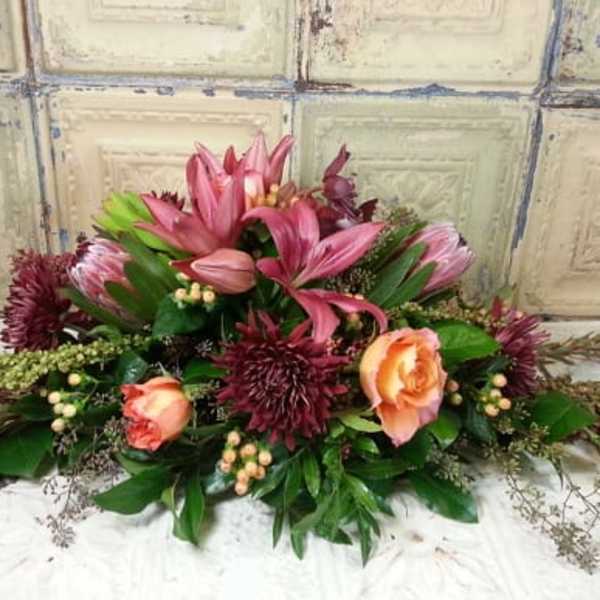 Low floral arrangement with pink lilies, peach roses, and burgundy blooms