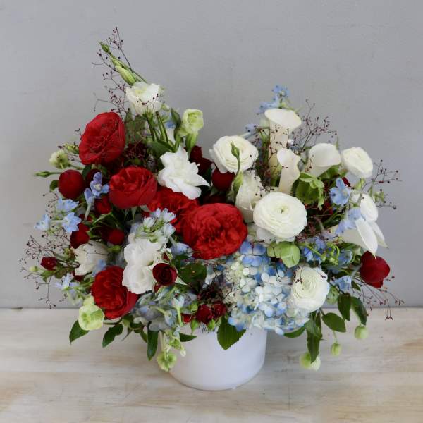 Red, white, and blue flower arrangement in a white ceramic vase