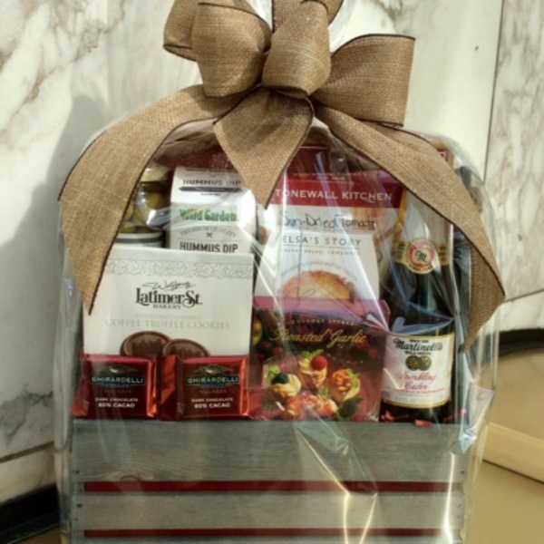 Gift basket with snacks, chocolates, and a bottle, wrapped in clear plastic with a large bow