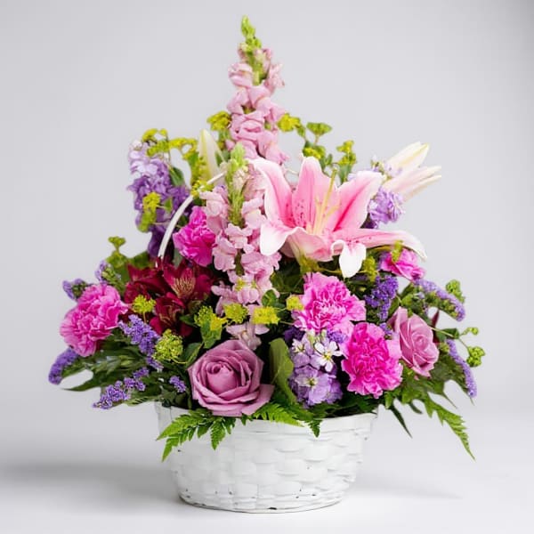 Pink and purple mixed flower arrangement in a white basket