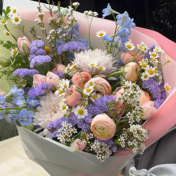 Pastel bouquet with pink ranunculus, white daisies, and blue flowers wrapped in pink paper
