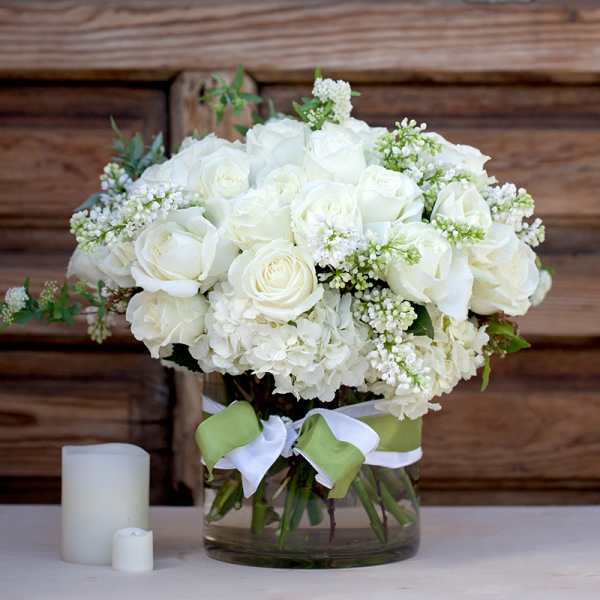 White roses and hydrangeas in a glass vase with a green ribbon