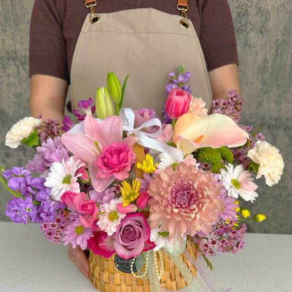 Pastel mixed flower arrangement in a woven basket with ribbon