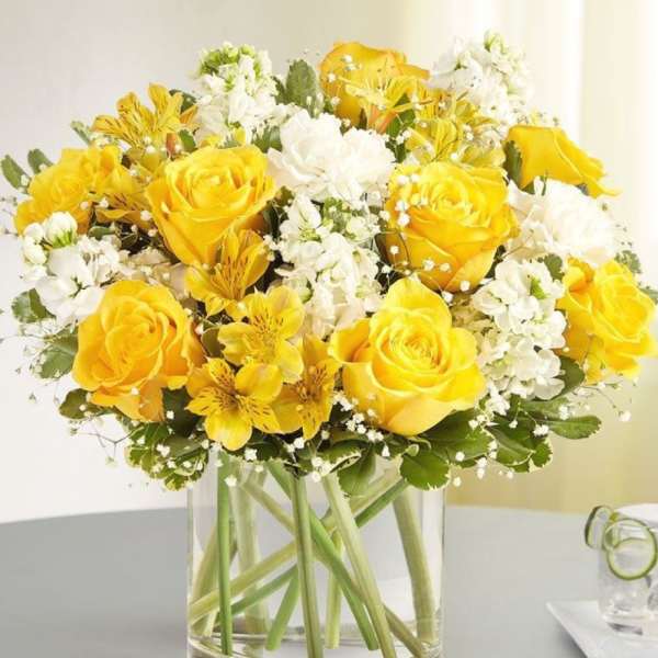 Yellow roses and white flowers arranged in a clear glass vase