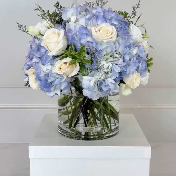 Blue hydrangea and white rose bouquet in a clear glass vase