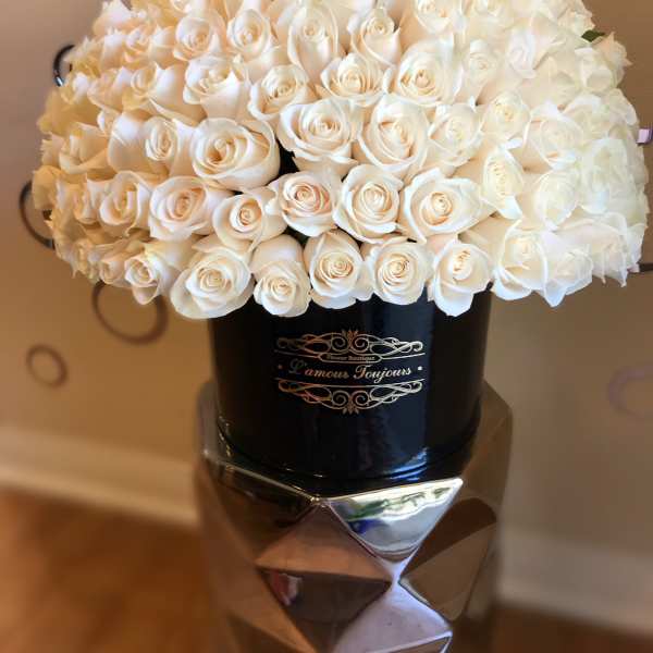 Dome of ivory roses arranged tightly in a black round hat box with gold lettering