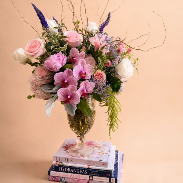 Mixed bouquet of pink roses, orchids, and white blooms in a glass vase