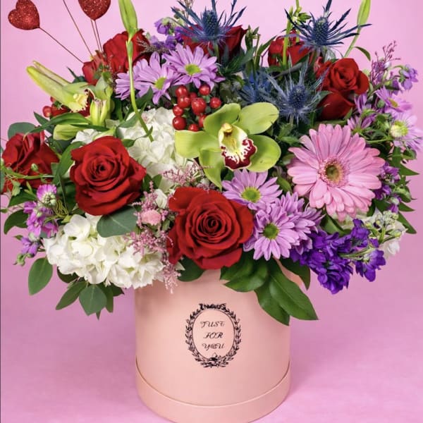 Mixed bouquet of red roses, pink daisies, and orchids in a pink hat box