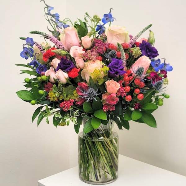 Mixed bouquet of pink, purple, and blue flowers in a clear glass vase