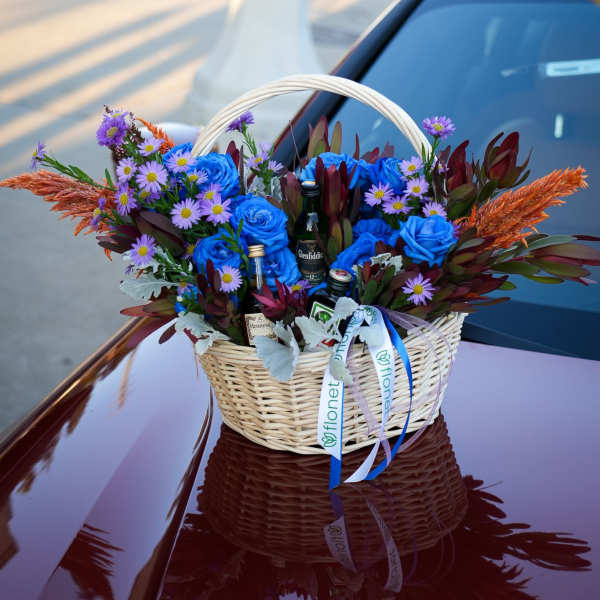 Basket arrangement with blue roses, purple daisies, and liquor bottles