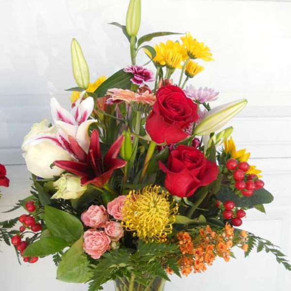 Mixed bouquet of red roses, lilies, and yellow flowers in a glass vase
