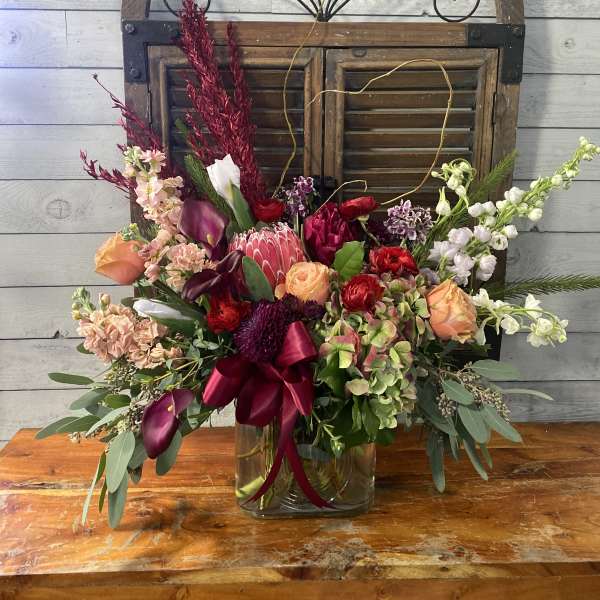 Mixed floral arrangement in a glass vase with burgundy ribbon