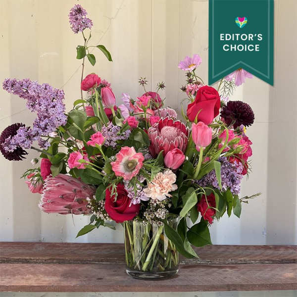 Mixed bouquet of pink, red, and lavender flowers in a glass vase