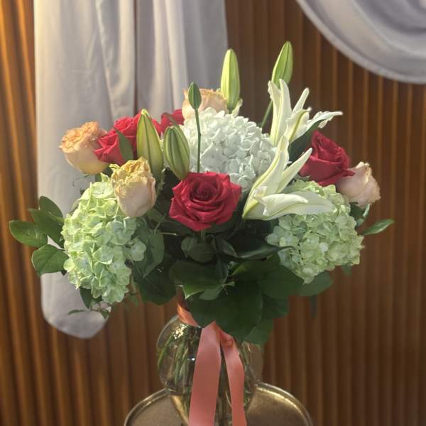 Bouquet of red and peach roses with white lilies and hydrangeas in a glass vase