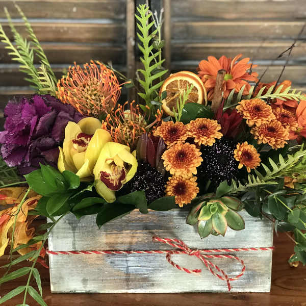Autumn floral arrangement in a wooden box with orange, yellow, and purple blooms