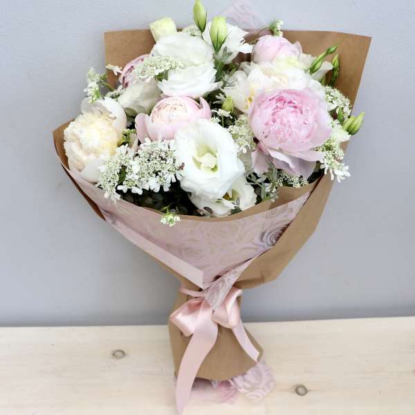 Hand-tied bouquet of white and pale pink peonies and lisianthus wrapped in kraft paper with a pink ribbon