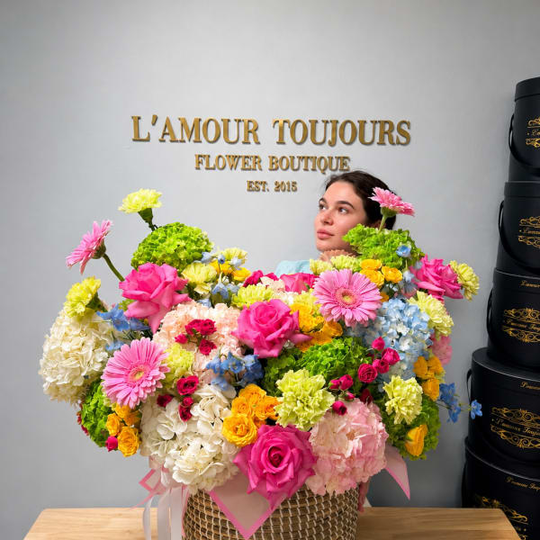 Large mixed flower arrangement in a woven basket with pink ribbon