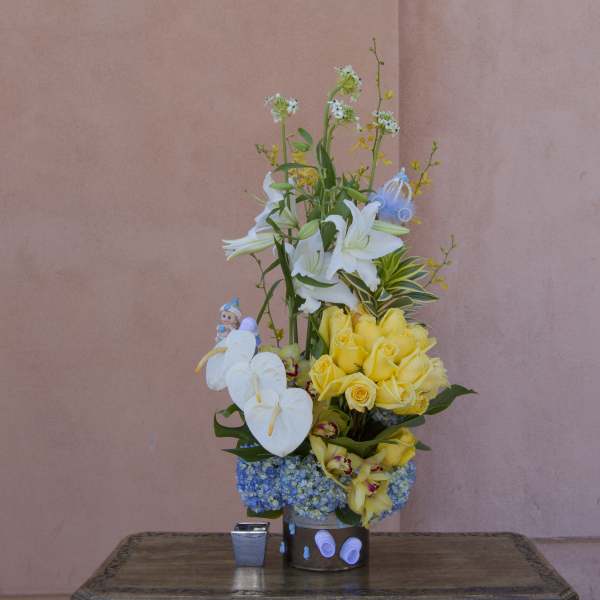 Tall floral arrangement with white lilies, yellow roses, and blue hydrangeas in a container