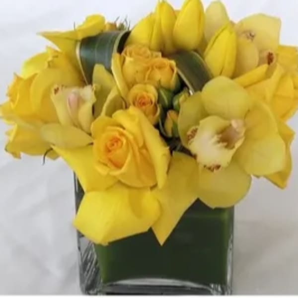 Yellow roses and orchids arranged in a square glass vase