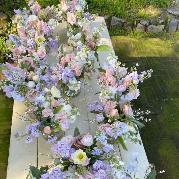 Pastel floral bouquets arranged in small glass vases on a long table outdoors.