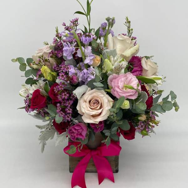 Mixed pink, red, and cream flower arrangement in a wooden cube with a bright pink bow.